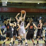 A basketball player in white jumps to shoot while surrounded by opposing players in black jerseys during a game.