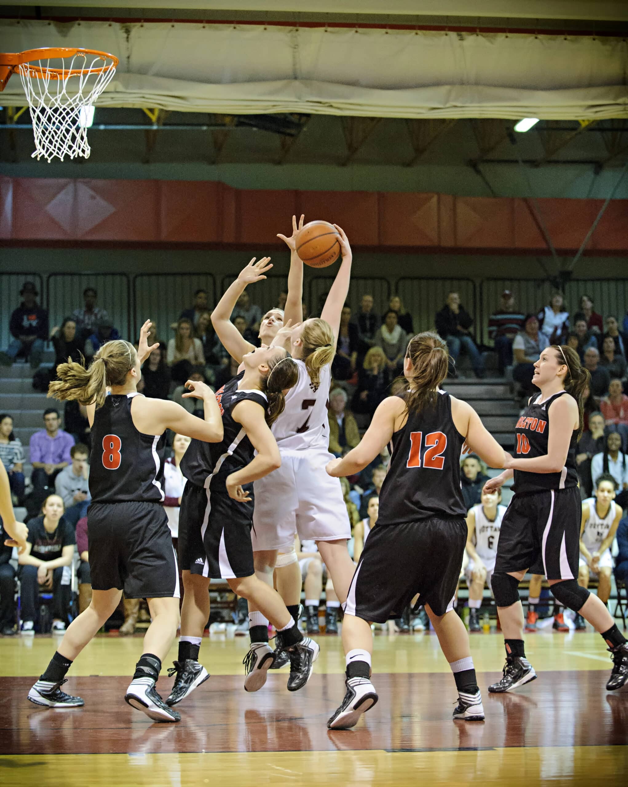 A basketball player in white jumps to shoot while surrounded by opposing players in black jerseys during a game.