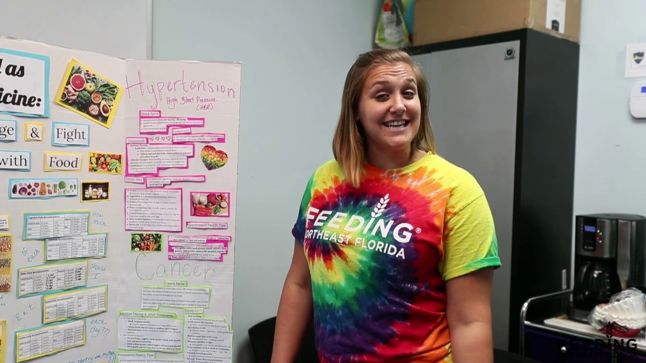 Person in a colorful tie-dye shirt standing next to a presentation board about hypertension.