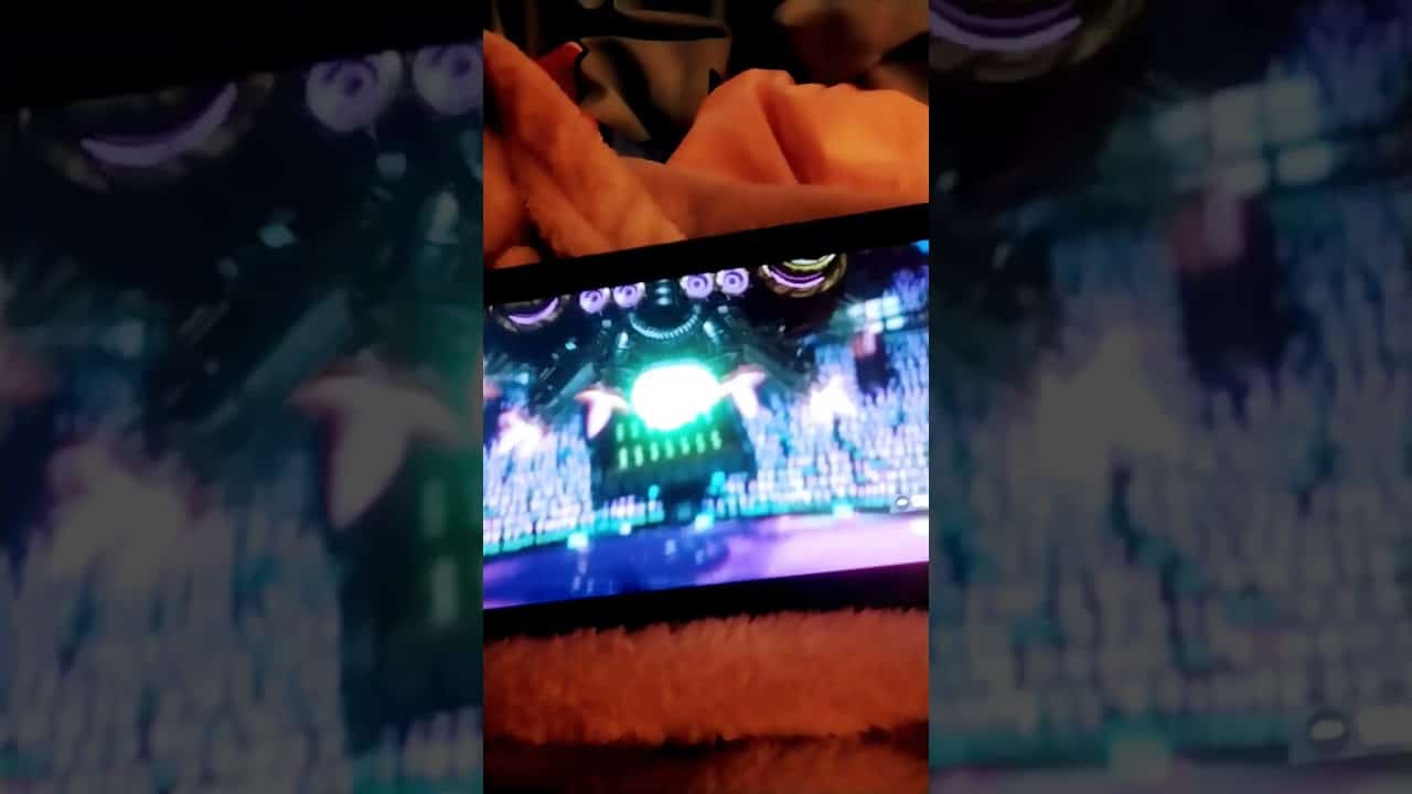 A smartphone screen displays a colorful video game scene featuring a large green creature in a dynamic environment.