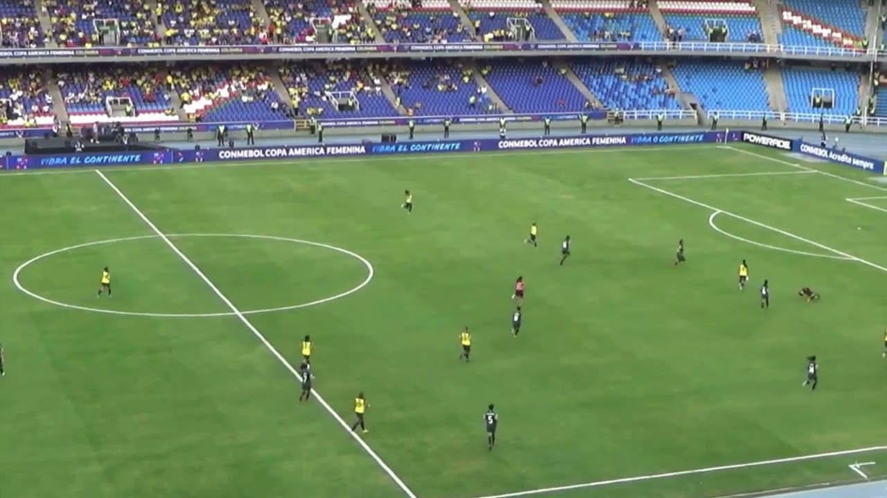 Soccer players on a green field during a match with scattered spectators in the stands.