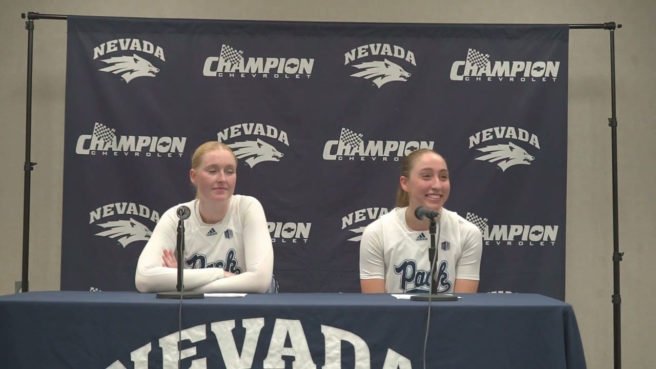 Two athletes in Nevada Wolf Pack jerseys sit at a press conference table with microphones, in front of a backdrop featuring "Nevada" and "Champion Chevrolet" logos.