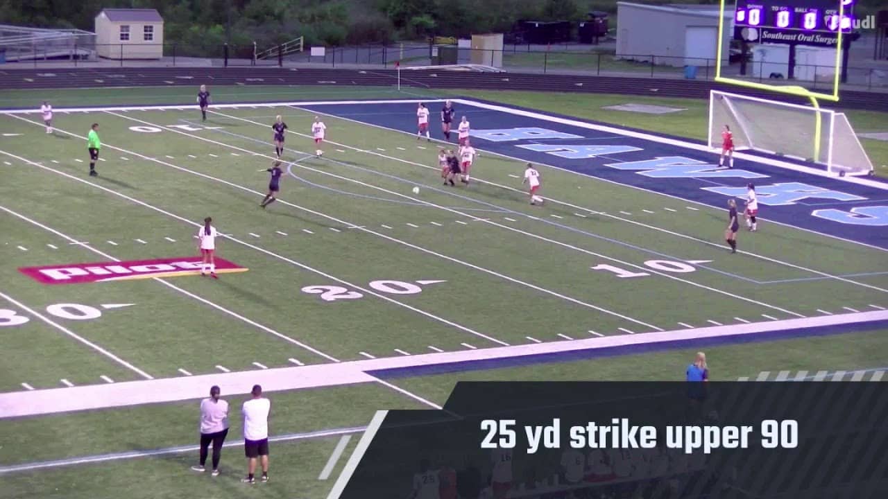 A soccer match on a field with players in mid-action near the goal. Text overlay reads "25 yd strike upper 90." Coaches stand on the sideline.