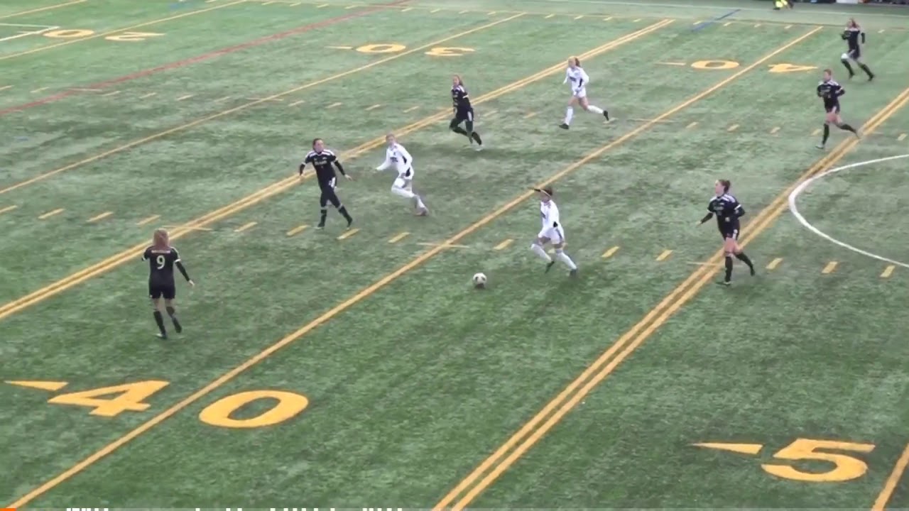 Soccer match in progress on a turf field; players in black and white jerseys are vying for the ball near the 40-yard line.