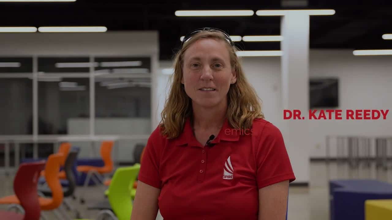 A person wearing a red shirt is seated indoors with colorful chairs in the background. The text "Dr. Kate Reedy" is written beside them.