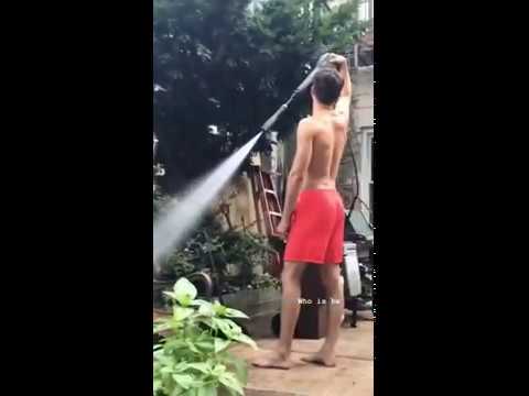 A person in red shorts stands outdoors holding a hose over their head, spraying water.