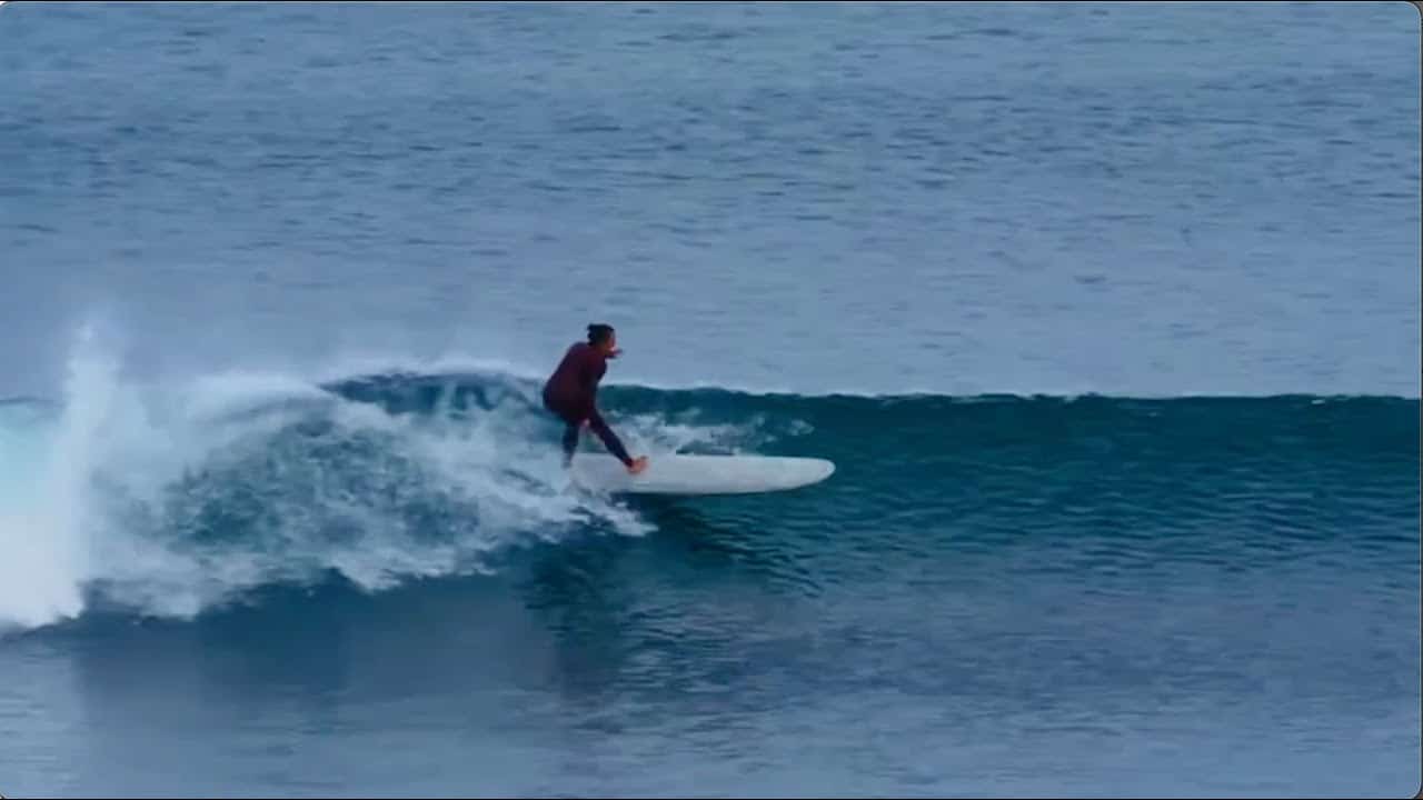 Person surfing on a blue wave with a longboard, wearing a dark wetsuit.