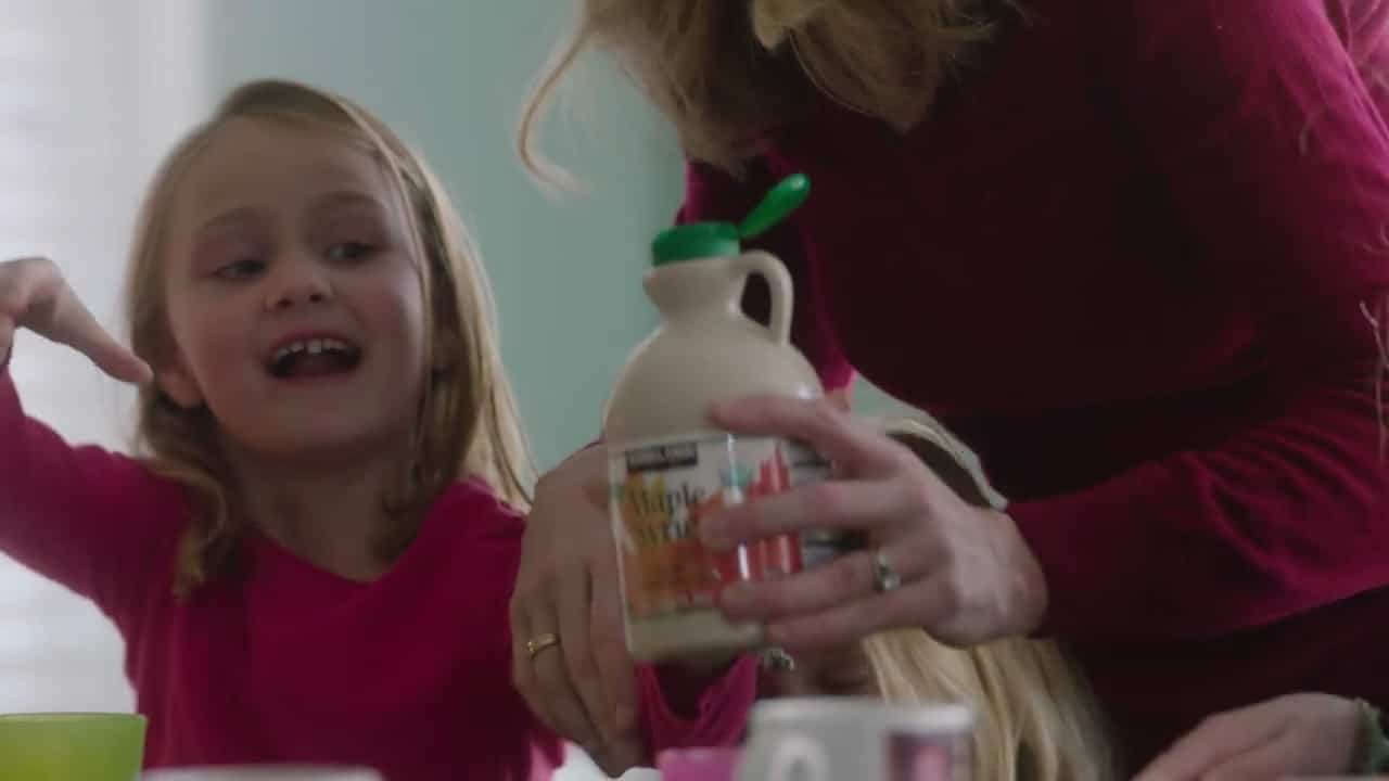 A child points at a bottle of maple syrup held by an adult at the table.