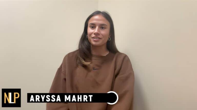 Aryssa Mahrt - Wisconsin NIL Amount, Net Worth, Player Information, Stats 4 A woman with long brown hair wearing a brown sweatshirt sits against a beige wall. Text at the bottom reads "NLP ARYSSA MAHRT.